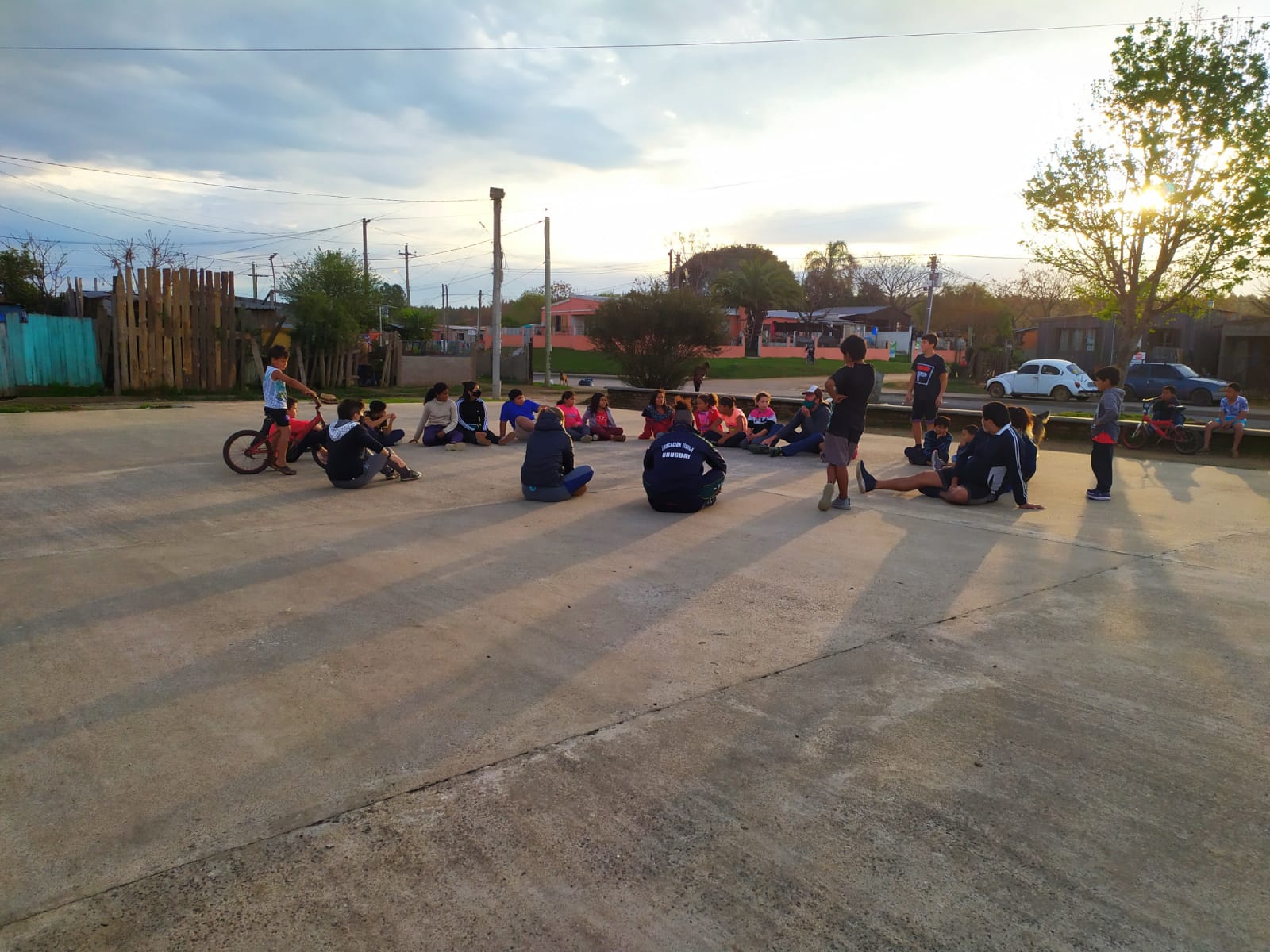 niñes, adolescentes y adultes sentandos en ronda en una plaza